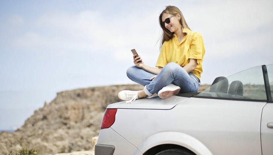young lady sitting at the back of her car holding her mobile phone
